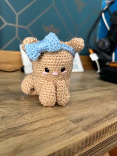 A small knitted teddy bear with a blue bow, positioned on a wooden surface.